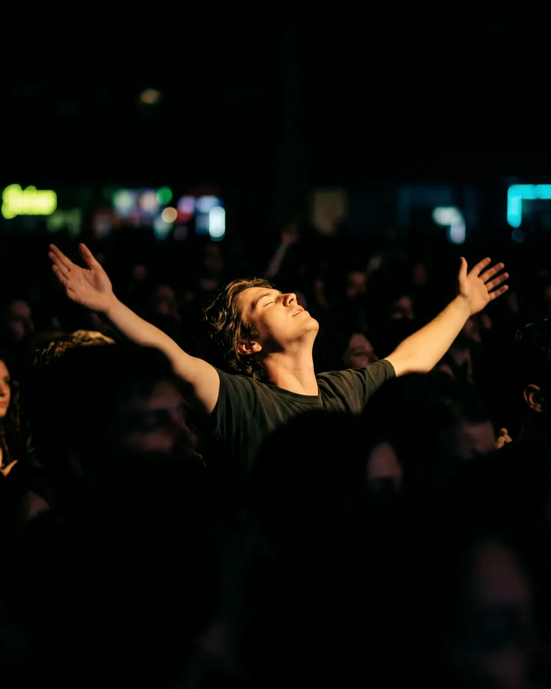 A fan in the crowd at night, head tipped back and arms wide open, lost in a fleeting moment